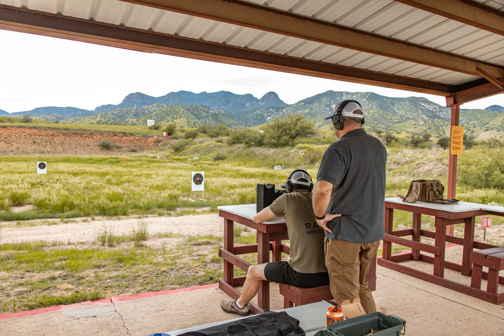 Instructor overseeing a student shooting a rifle from a bench at a Cochise County range